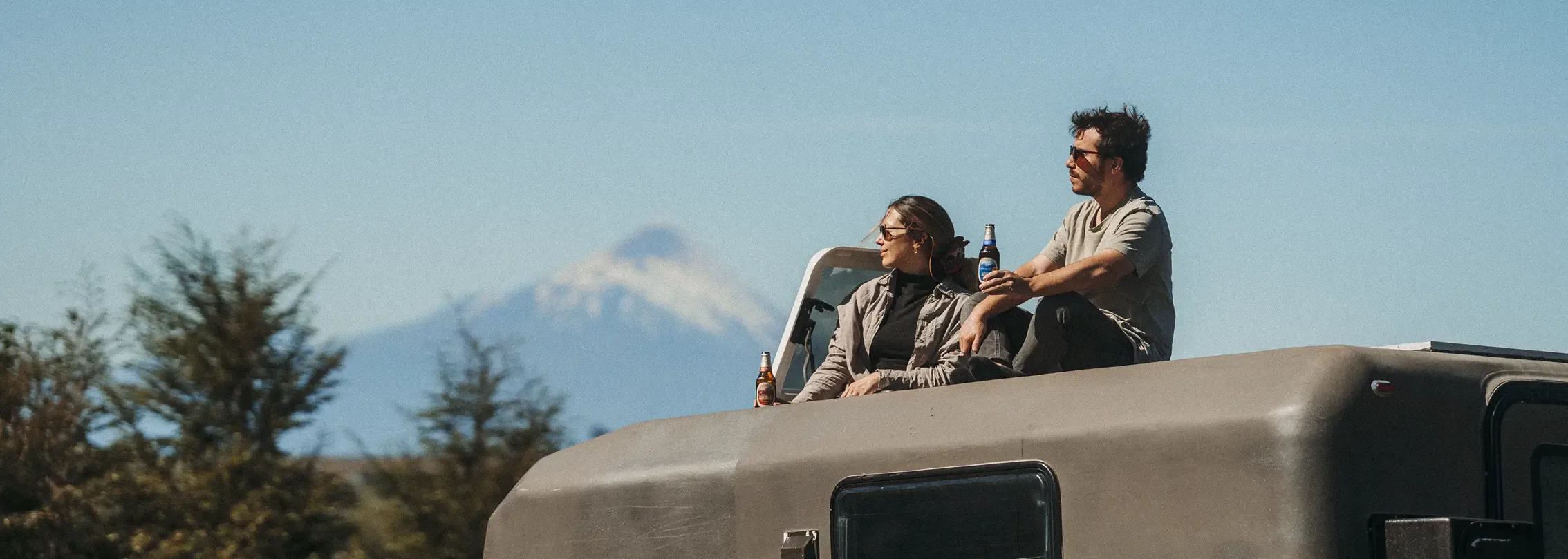 Couple sitting on a camper's roof facing the volcano