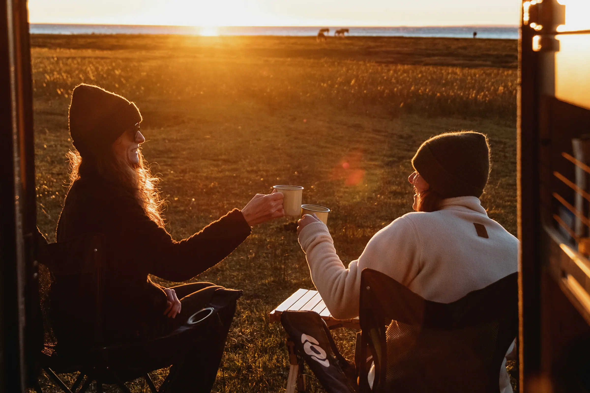 Two travellers having coffee at sunset by the camper